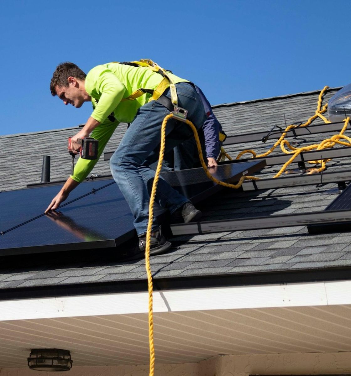 Técnico com equipamento de segurança instalando painéis solares em um telhado
